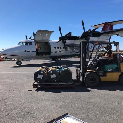 A forklift positioning drums beside an Air Tindi aircraft
